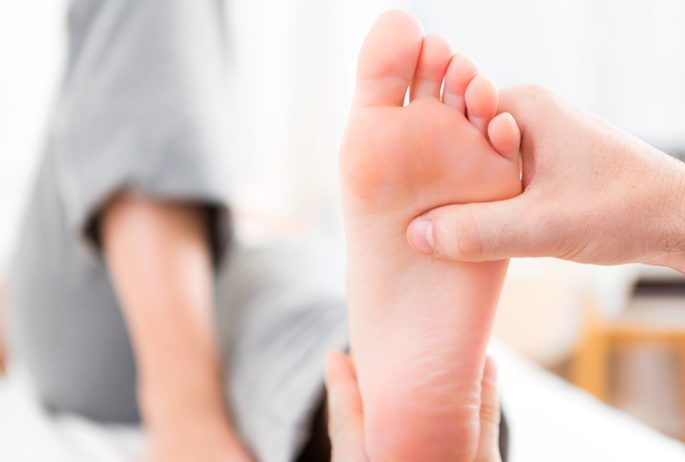 View of a Young attractive physiotherapist doing reflexology on a patient feet